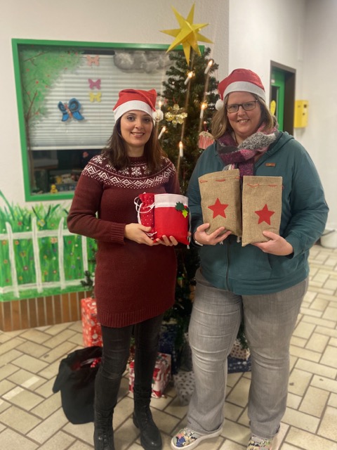Zwei Frauen mit Nikolausmützen und Geschenken vor einem Tannenbaum